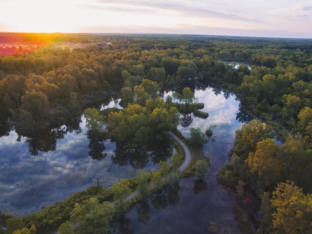 High angle drone photo of trees beside a river at sunset in Michigan