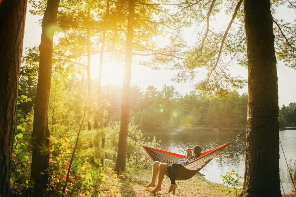 Two people relaxing together on a gray hammock beside trees at a Michigan campsite