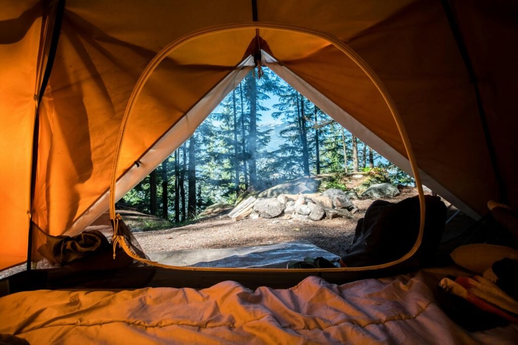 Orange camping tent pitched in a forest campsite surrounded by green trees
