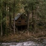 Rustic cabin beside a flowing river in the woods, representative of Two Rivers Ozark Cabins