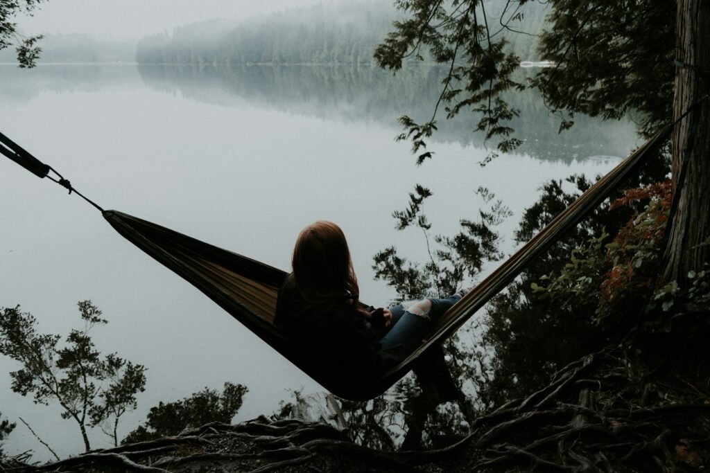 Woman sitting alone on a hammock facing away, in a quiet misty forest